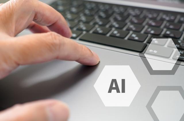 ノートパソコンを操作する手元とAIの文字